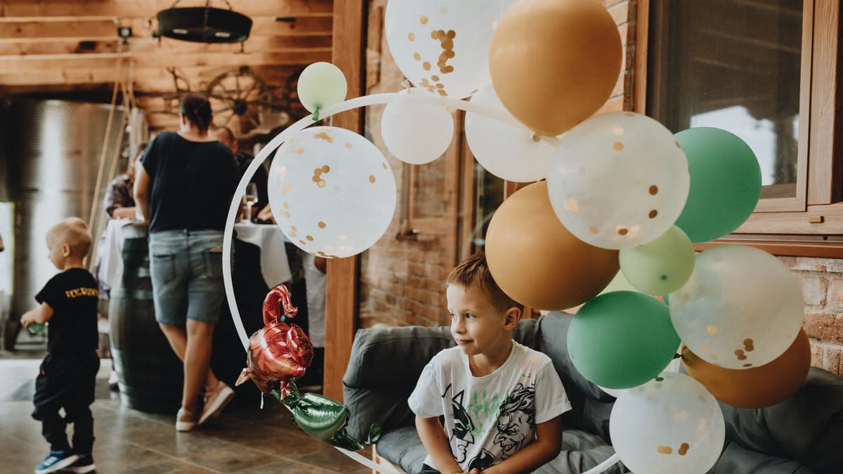 A young boy with balloons at an indoor birthday party gathering.