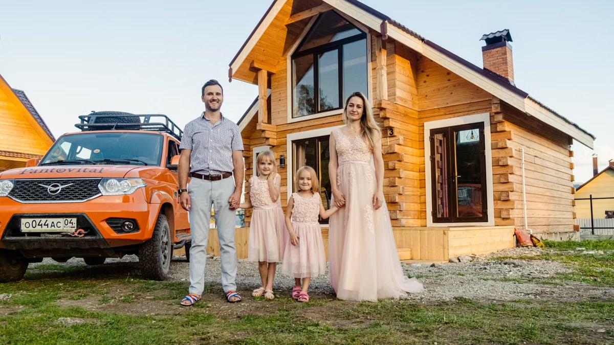 Family of four happily standing outside their modern wooden house on a sunny day.